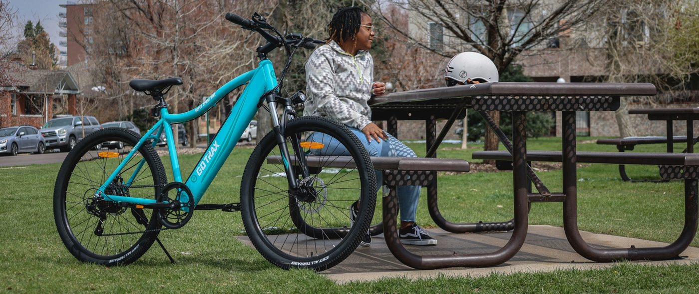 Approachable rider beside a teal step-through e-bike in a park setting